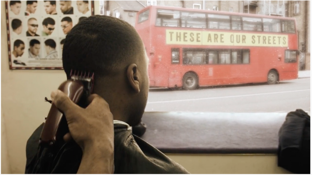 Man in barbers looking out of the window with a red bus in the background showing the text these are our streets on the side